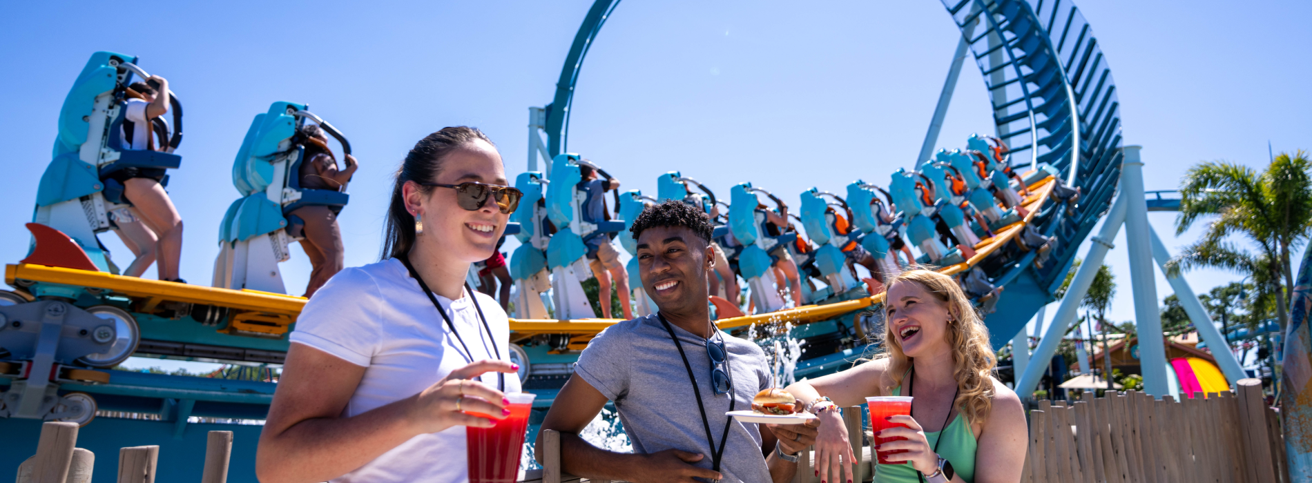 Three people in front of a roller coaster with food and drinks